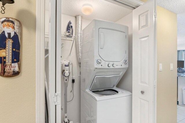 laundry room with stacked washer / dryer, a textured ceiling, and tile patterned flooring