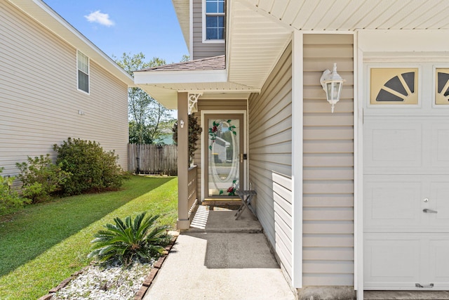 property entrance featuring a yard, an attached garage, and fence