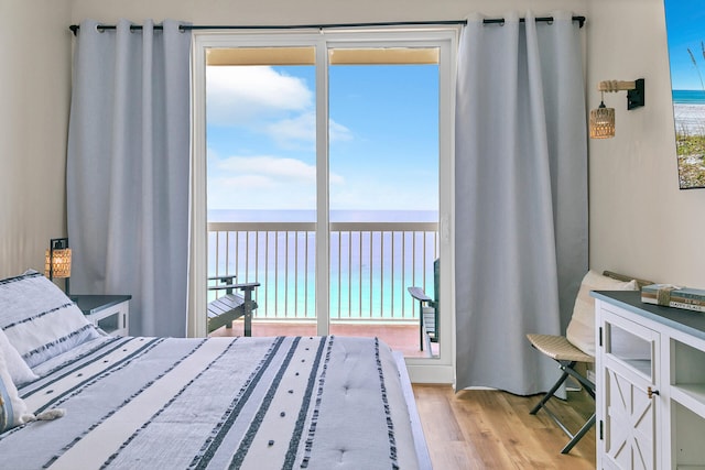 bedroom with multiple windows, light hardwood / wood-style flooring, a view of the beach, and a water view