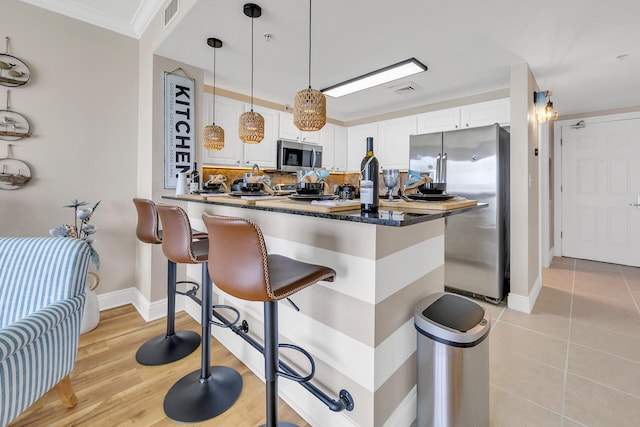 kitchen featuring pendant lighting, stainless steel appliances, a kitchen breakfast bar, tasteful backsplash, and white cabinets