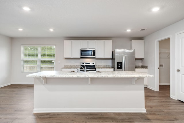 kitchen with light wood-type flooring, stainless steel appliances, an island with sink, and white cabinetry