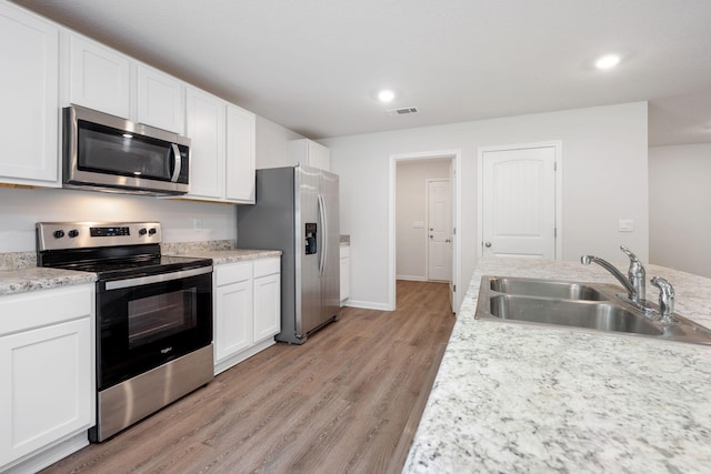 kitchen with appliances with stainless steel finishes, light stone countertops, light wood-type flooring, sink, and white cabinetry