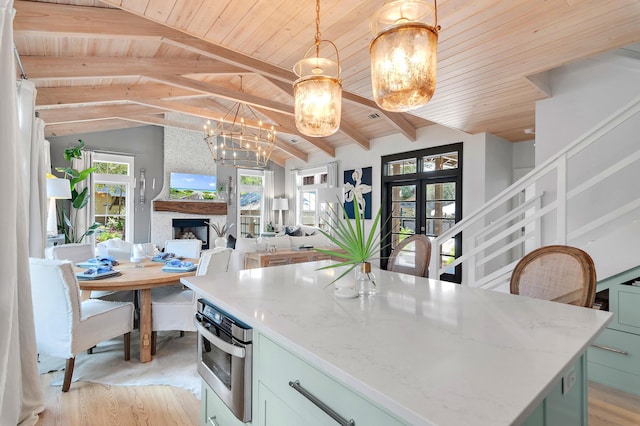 kitchen featuring decorative light fixtures, vaulted ceiling with beams, a large fireplace, stainless steel oven, and wooden ceiling