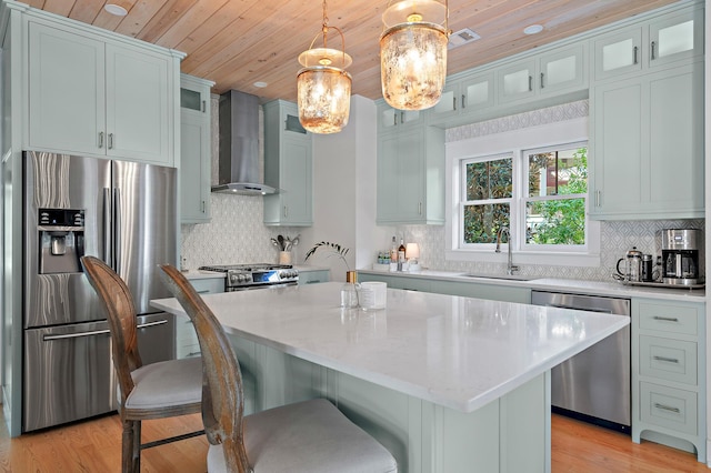 kitchen featuring wall chimney exhaust hood, appliances with stainless steel finishes, a breakfast bar, pendant lighting, and a sink