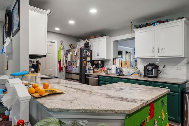 kitchen featuring white cabinets, decorative backsplash, black fridge, light stone counters, and green cabinetry