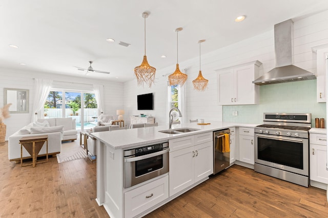 kitchen with stainless steel appliances, hardwood / wood-style floors, wall chimney range hood, sink, and backsplash