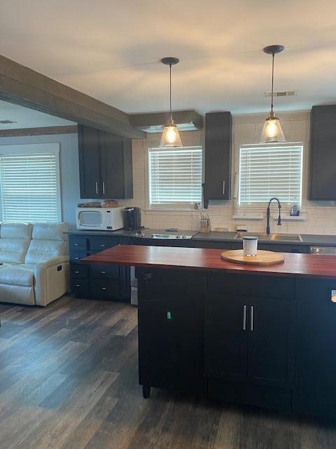 kitchen with sink, backsplash, hanging light fixtures, and dark wood-type flooring