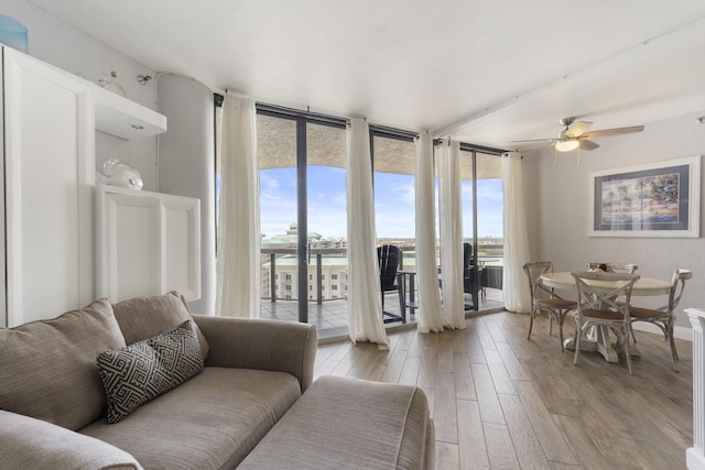 living area featuring expansive windows, a water view, a ceiling fan, and light wood-style floors