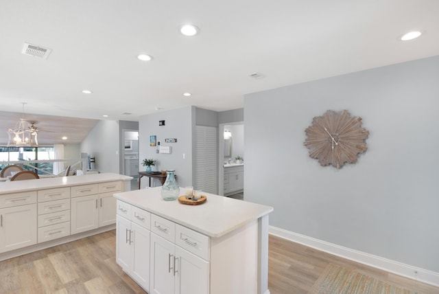 kitchen with white cabinetry, decorative light fixtures, a center island, and light hardwood / wood-style flooring