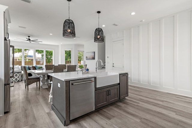 kitchen with stainless steel appliances, a kitchen island with sink, light hardwood / wood-style floors, hanging light fixtures, and sink