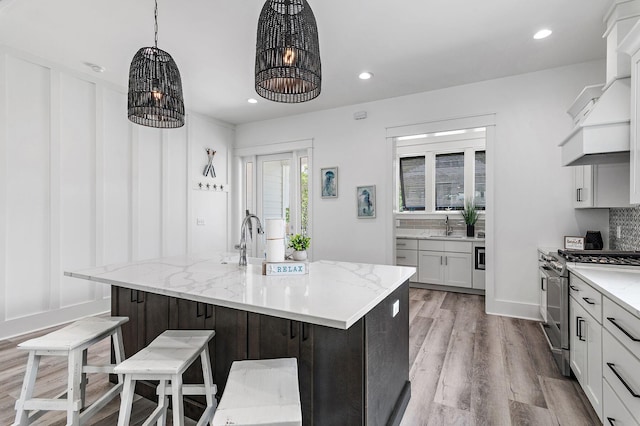 kitchen featuring light hardwood / wood-style flooring, an island with sink, light stone counters, and high end stainless steel range oven