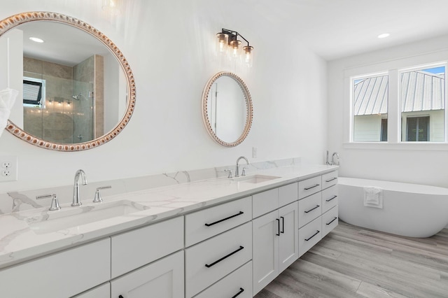 bathroom with dual bowl vanity, wood-type flooring, and independent shower and bath