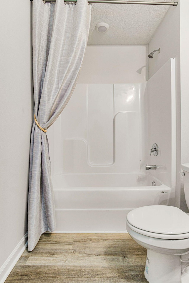 bathroom with shower / bath combination with curtain, wood-type flooring, a textured ceiling, and toilet