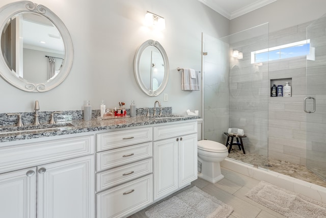 bathroom with double sink vanity, toilet, crown molding, and a shower with shower door