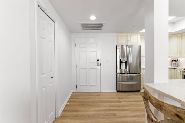 kitchen featuring light hardwood / wood-style floors, light stone counters, cream cabinets, and stainless steel refrigerator with ice dispenser