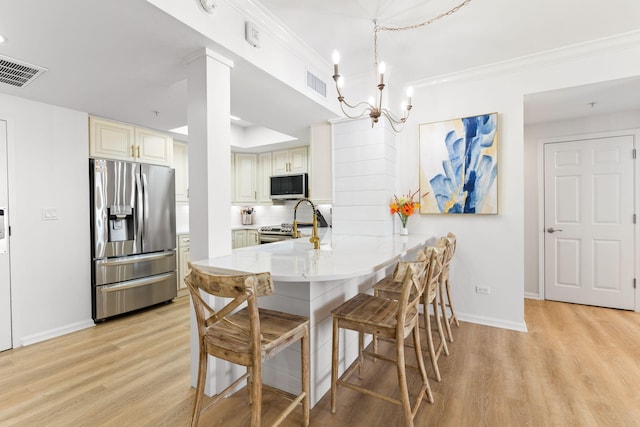 kitchen featuring appliances with stainless steel finishes, a breakfast bar, decorative light fixtures, light hardwood / wood-style floors, and ornamental molding