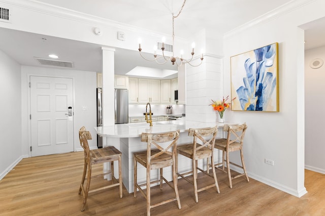 kitchen featuring kitchen peninsula, decorative light fixtures, light hardwood / wood-style floors, appliances with stainless steel finishes, and a kitchen bar