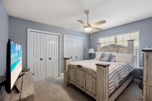 bedroom featuring ceiling fan, two closets, and light colored carpet