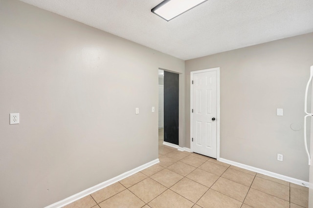 empty room featuring light tile patterned flooring, a textured ceiling, and baseboards