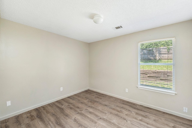 unfurnished room featuring baseboards, visible vents, a textured ceiling, and light wood finished floors