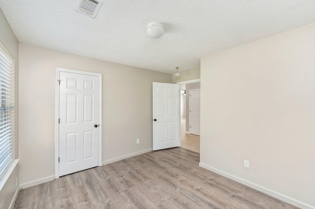 unfurnished bedroom with light wood-style floors, baseboards, visible vents, and a textured ceiling