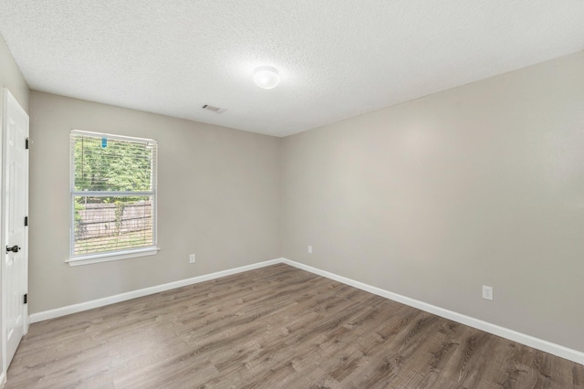 empty room featuring visible vents, a textured ceiling, baseboards, and wood finished floors