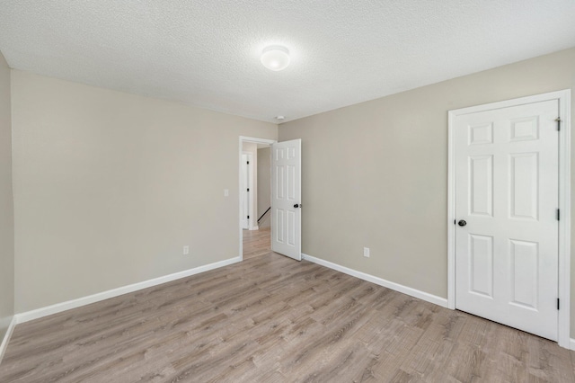 spare room featuring light wood-style flooring, baseboards, and a textured ceiling