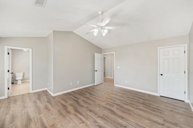 unfurnished bedroom with lofted ceiling, ensuite bathroom, light wood-type flooring, and ceiling fan