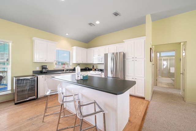 kitchen with sink, white appliances, white cabinetry, wine cooler, and a kitchen island