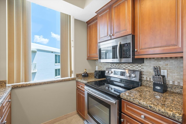 kitchen with stainless steel appliances, brown cabinetry, and dark stone countertops