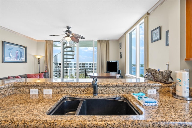 kitchen with crown molding, stone countertops, open floor plan, a sink, and ceiling fan