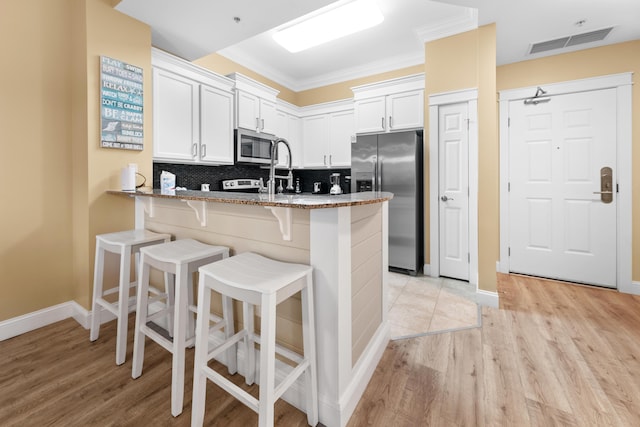 kitchen featuring kitchen peninsula, a breakfast bar, stone counters, appliances with stainless steel finishes, and white cabinets