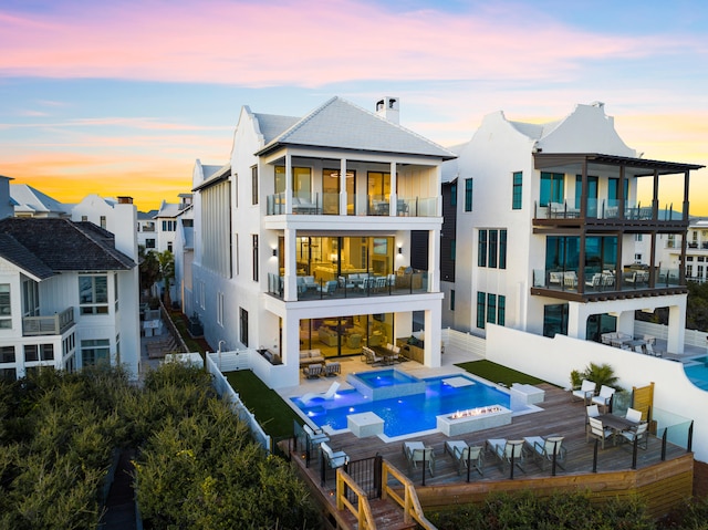 back house at dusk with a balcony and a fenced in pool