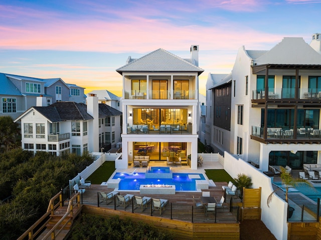 back house at dusk featuring a pool side deck, an outdoor hangout area, and a balcony