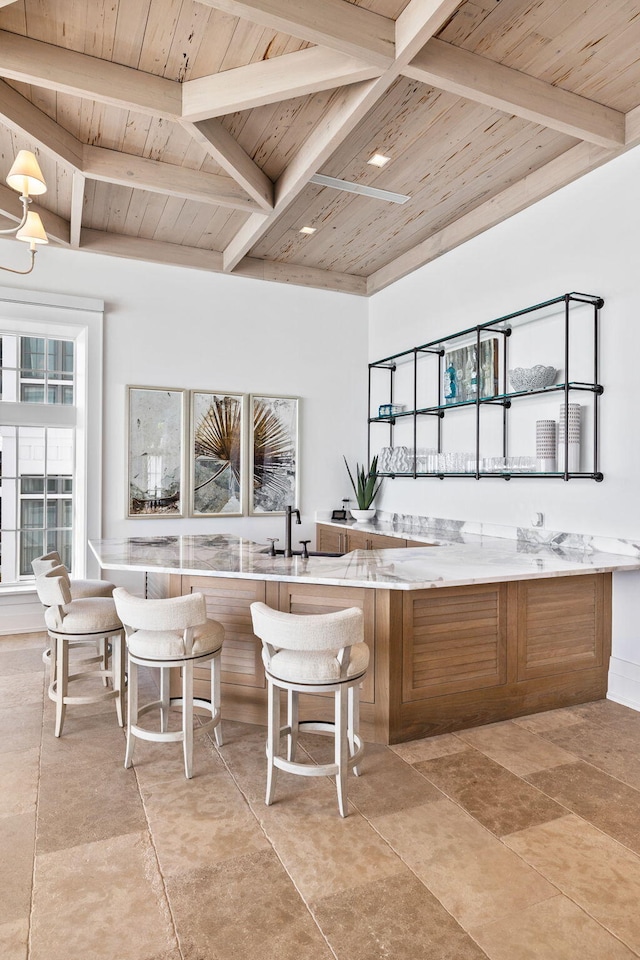 kitchen with wooden ceiling, beam ceiling, light stone counters, light tile patterned floors, and sink