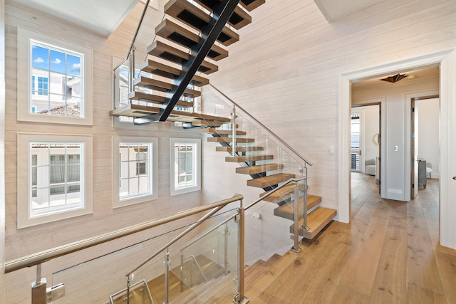 stairway featuring a wealth of natural light, wooden walls, and light hardwood / wood-style floors