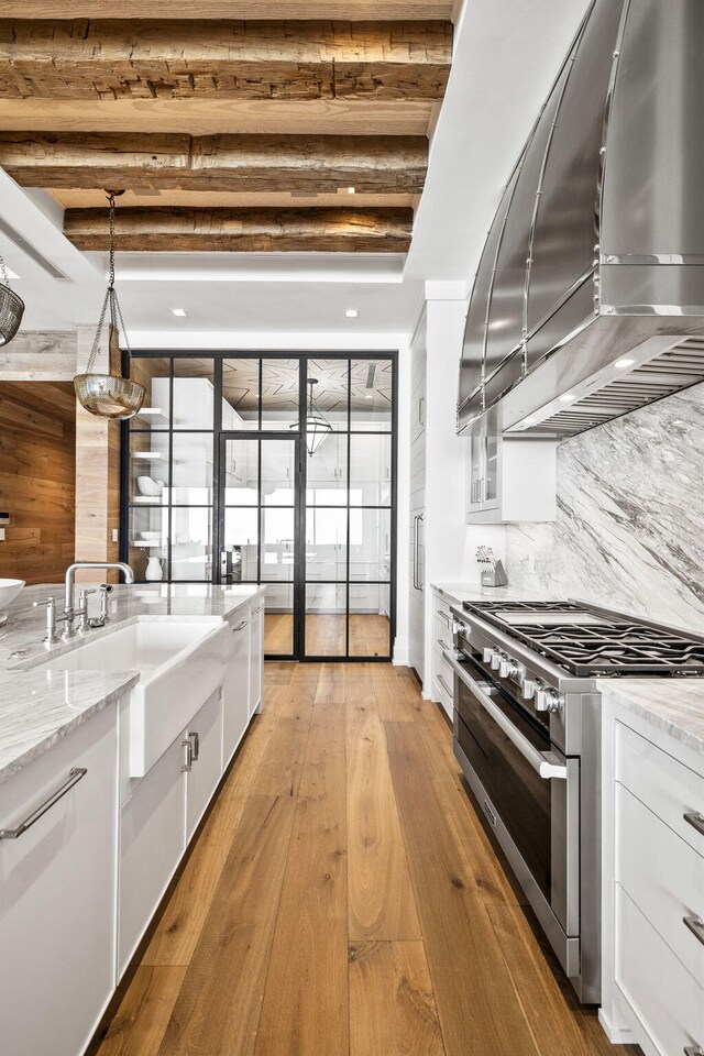 kitchen featuring high end stainless steel range oven, wall chimney exhaust hood, white cabinets, and decorative light fixtures