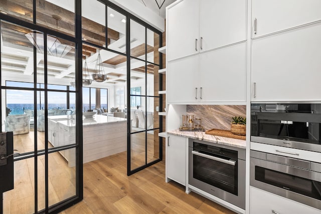 kitchen featuring backsplash, stainless steel oven, white cabinetry, and light hardwood / wood-style flooring