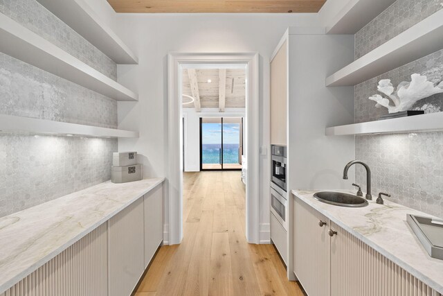 kitchen featuring wood ceiling, light wood-type flooring, light stone counters, and sink