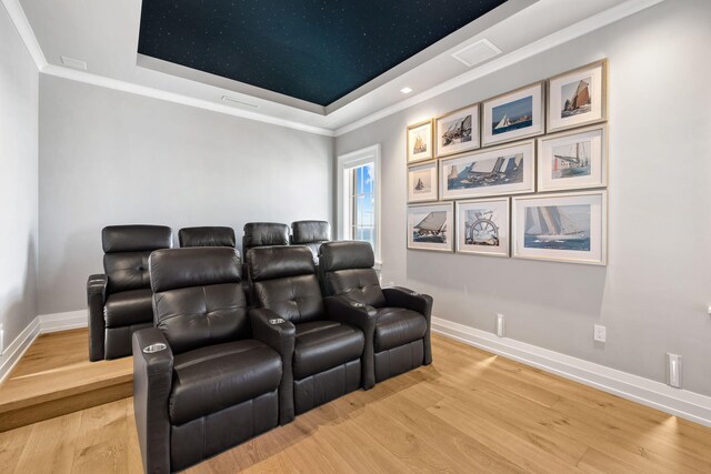 home theater room with light wood-type flooring and a raised ceiling