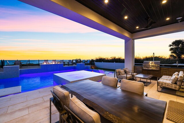 patio terrace at dusk featuring grilling area, exterior kitchen, a water view, and an outdoor living space