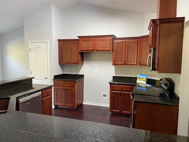 kitchen with dark hardwood / wood-style floors, dark stone countertops, stainless steel appliances, and vaulted ceiling