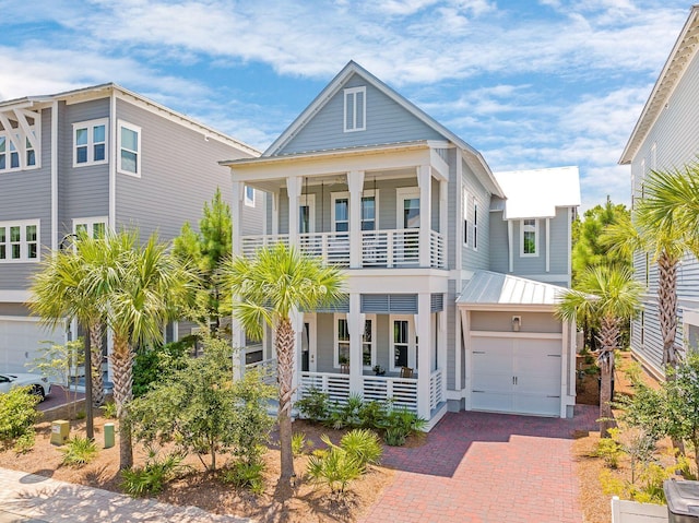 beach home featuring a standing seam roof, decorative driveway, covered porch, metal roof, and a balcony