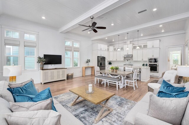 living area with beam ceiling, light wood-style flooring, visible vents, and ornamental molding