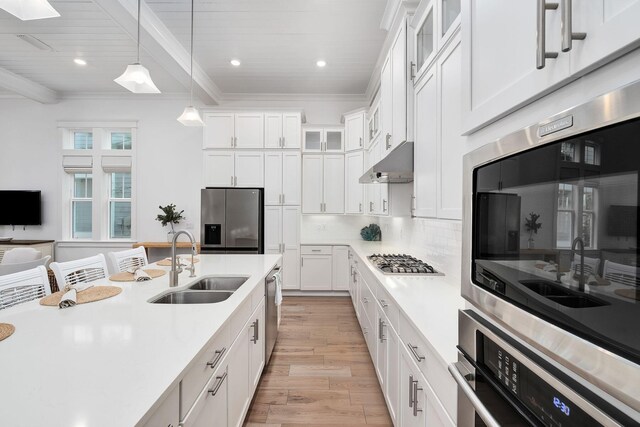 kitchen featuring under cabinet range hood, decorative light fixtures, a sink, stainless steel appliances, and light countertops