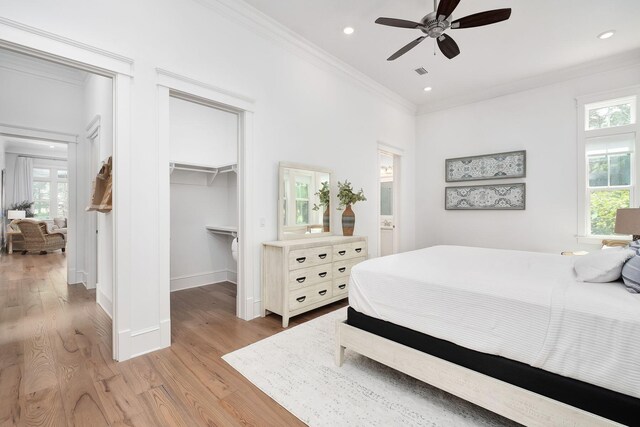 bedroom with a walk in closet, recessed lighting, light wood-style floors, crown molding, and baseboards