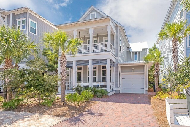 coastal inspired home with decorative driveway, a balcony, a porch, and a garage