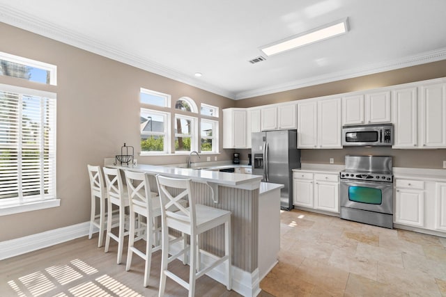 kitchen with light tile patterned floors, appliances with stainless steel finishes, a kitchen breakfast bar, ornamental molding, and white cabinetry