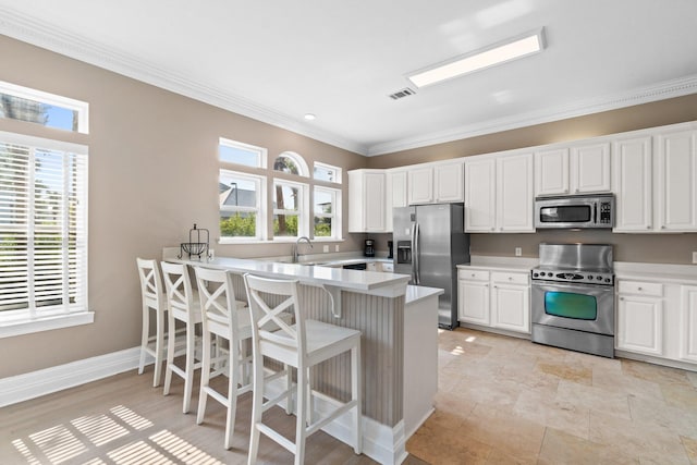 kitchen featuring appliances with stainless steel finishes, white cabinetry, sink, a kitchen bar, and kitchen peninsula