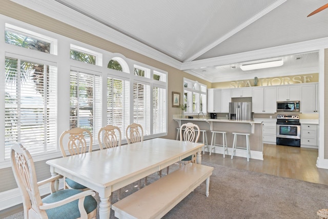 dining room with ornamental molding, vaulted ceiling, and light hardwood / wood-style floors